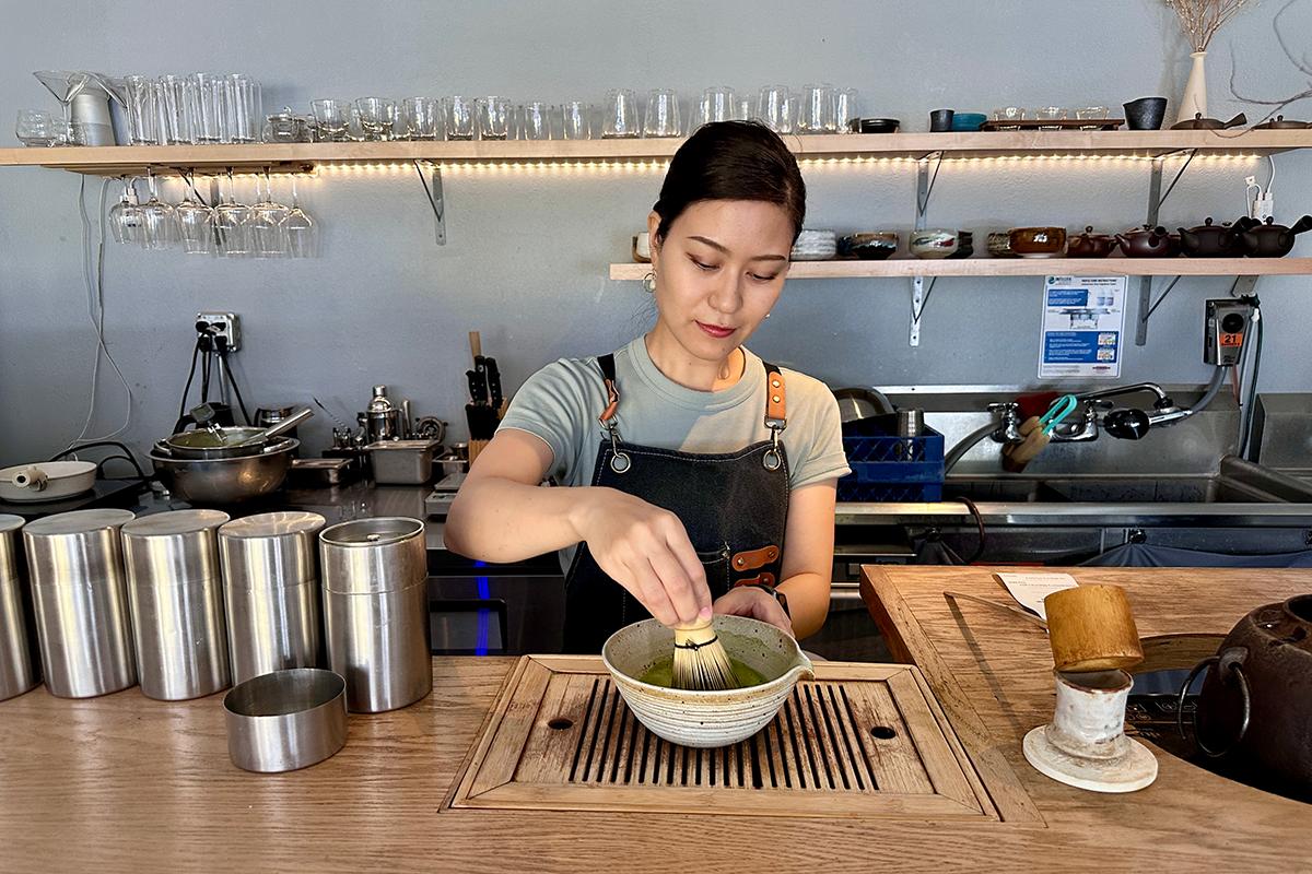 Tea professional whisking matcha with a bamboo whisk at a café counter